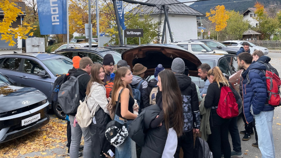 Verschiedene Schülerinnen und Schüler stehen vor einer geöffneten Motorhaube